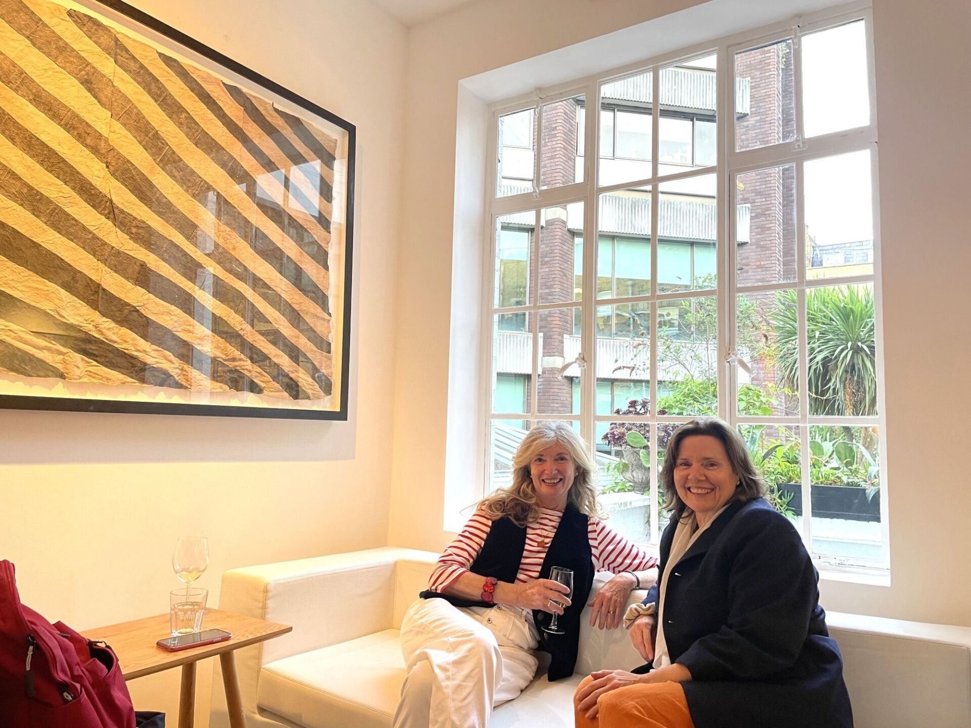 Two alumni sit in front of a window at the Rebecca Hossack Art Gallery, London.