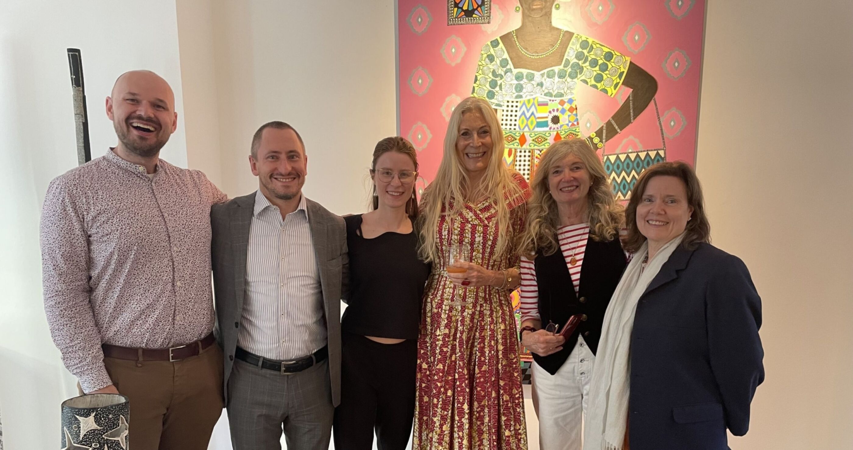 Six Burgmann alumni and friends stand together in front of an artwork at the Rebecca Hossack Art Gallery, London.