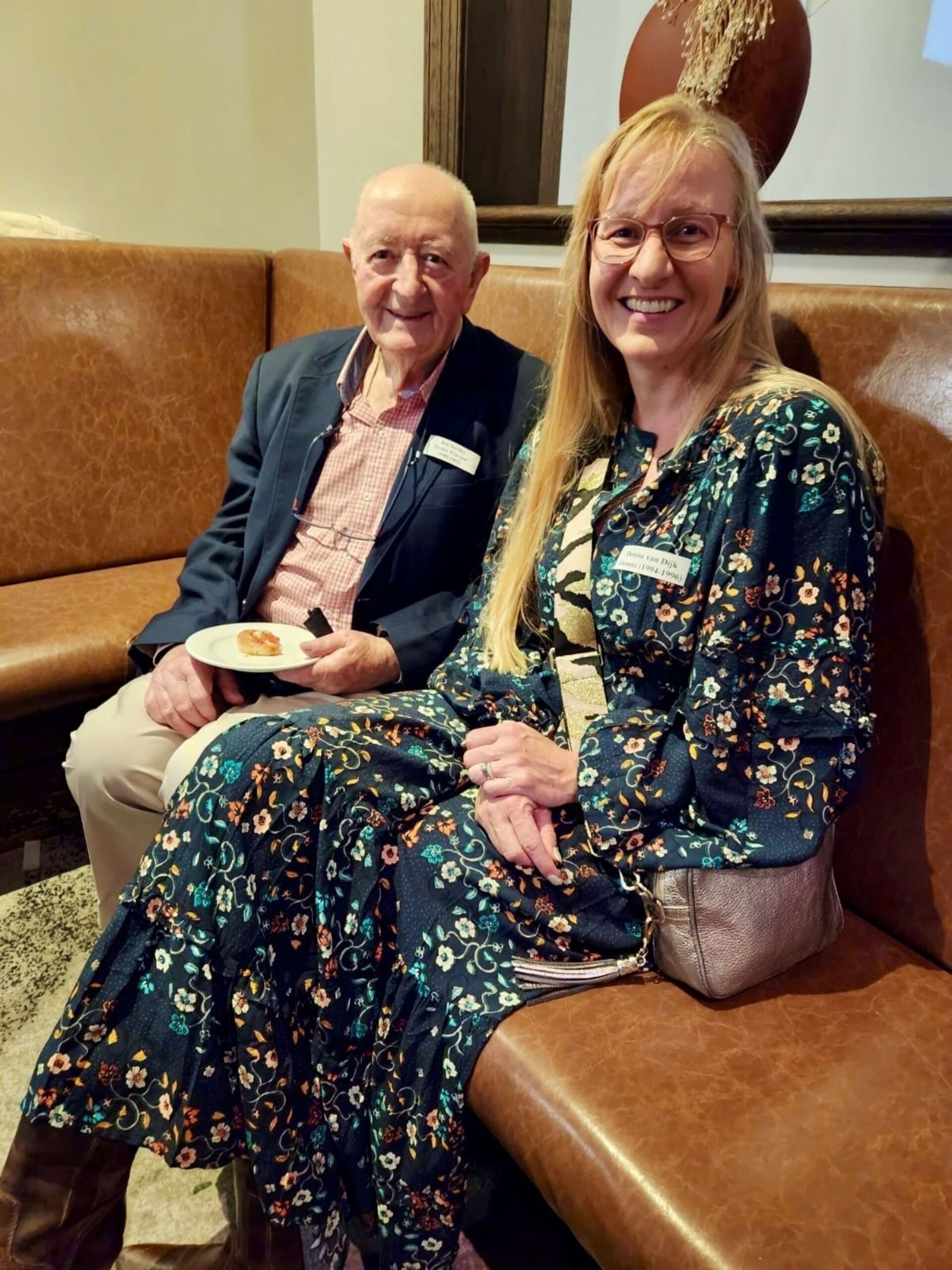 Two Burgmann alumni sit together on a brown lounge at the 2024 Melbourne event.