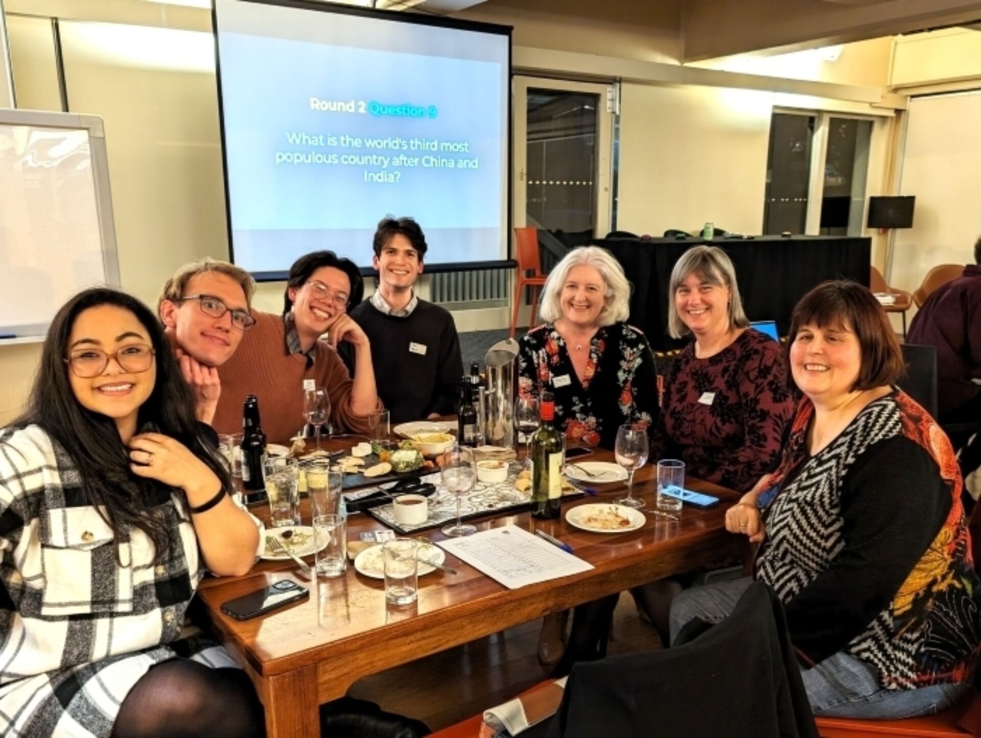 A photograph of Burgmann College alumni and staff sitting around a table with refreshments at the 2024 Trivia Night.