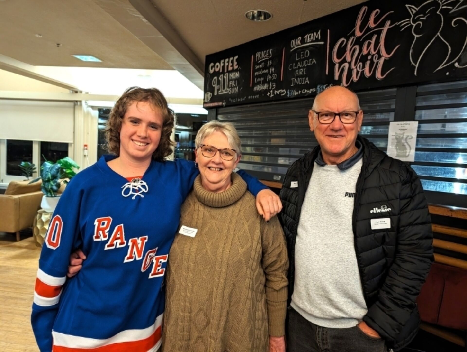 A photograph of three people standing together in front of Le Chat Noir, Burgmann College.
